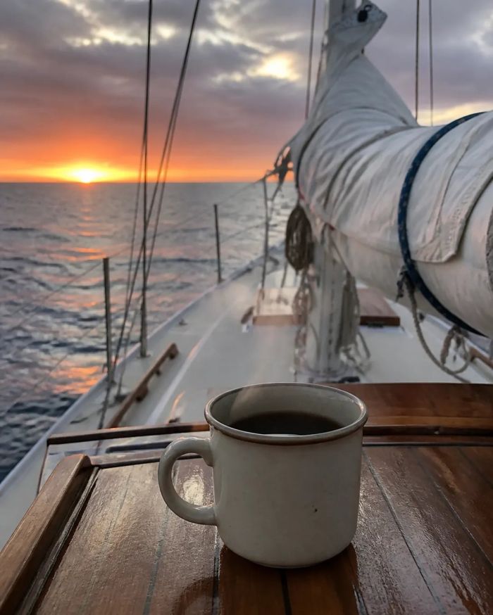 A mug of coffee on the deck of a sailboat at sunset