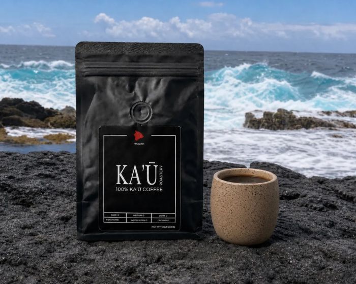 A bag of Kaʻū Roastery coffee on black lava rock beside the ocean
