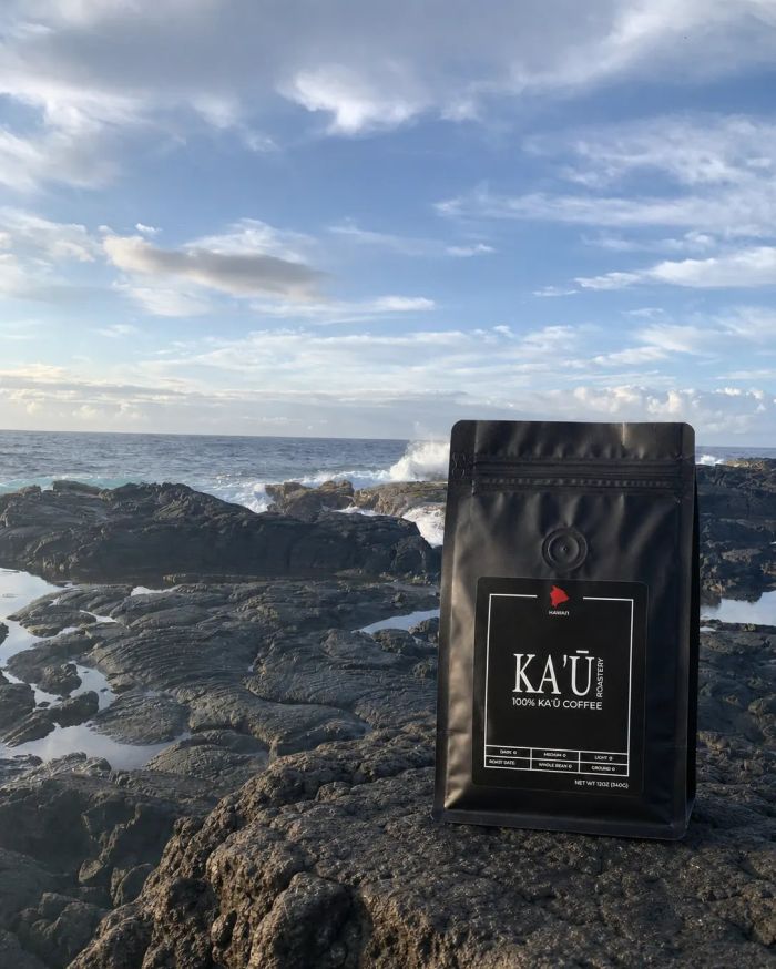 A bag of Kaʻū Roastery coffee on lava rock above the ocean